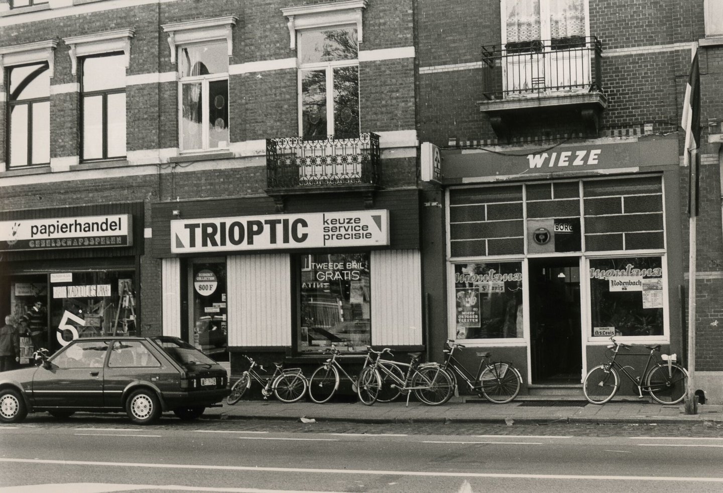 Straatbeeld met gevel van optiekzaak Trioptic een papierhandel en café Montana in Gent