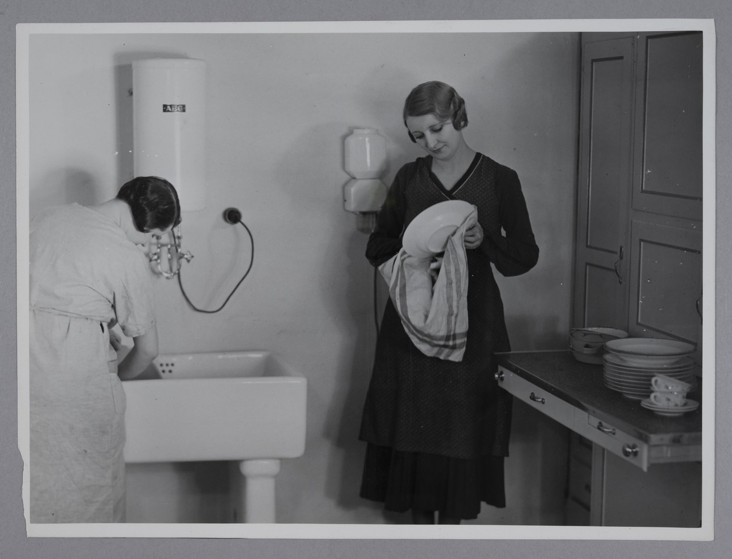 Vrouwen doen de afwas in de keuken met aan de muur een elektrische boiler van het merk AEG