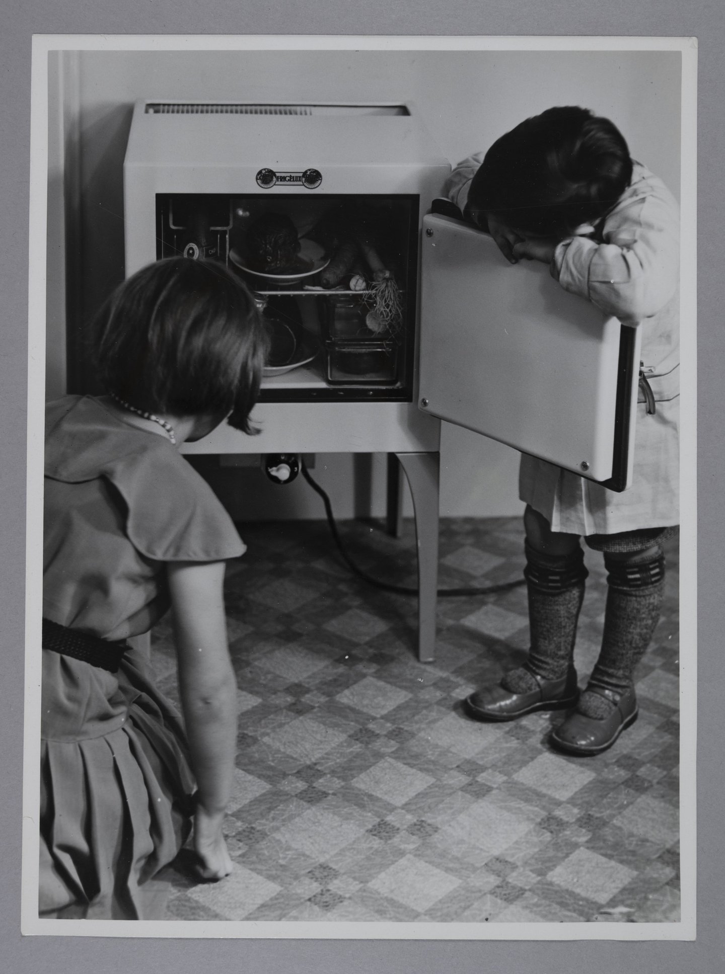 Kinderen kijken in een kleine elektrische koelkast van het merk Frigèlux